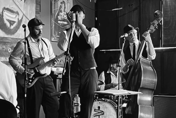 Band performs indoors with singer guitarist bassist and drummer creating classic jazz vibe.
