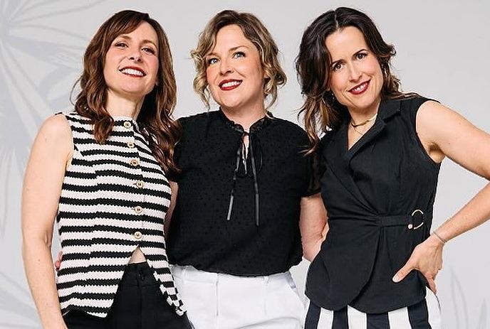 Three group members wearing monochrome outfits stand together while smiling.