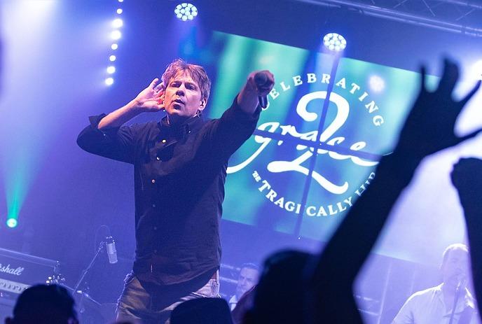 A male singer from 'Grace 2 – Celebrating the Tragically Hip' performs energetically on stage.