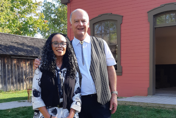 Denise Pelley and Stephen Holowitz pose for a photo outside of a building at the Fanshawe Pioneer Village on a sunny day.