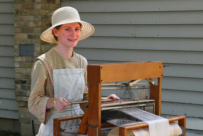Woman demonstrating traditional weaving on a wooden loom outdoors.
