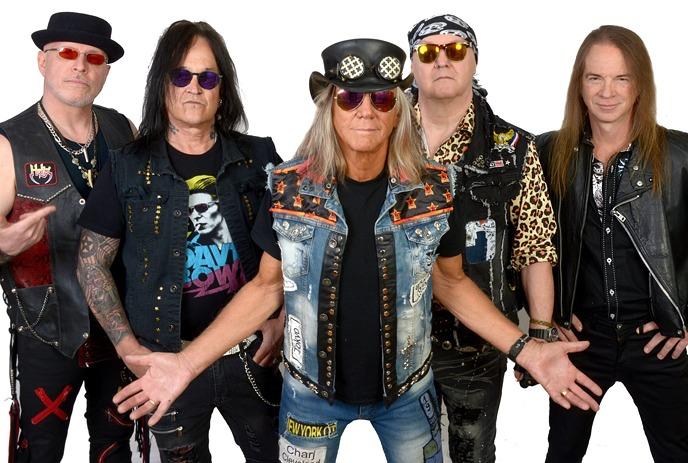 Three rock musicians performing under the spotlight on the stage with crowd cheering.