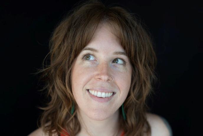 Hilary Watson looking upward softly lit against dark backdrop in close portrait.