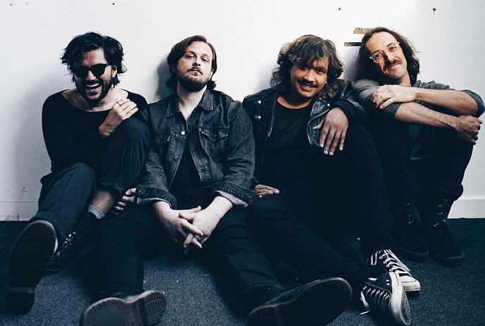 The 4 band members of Hotel Mira, sitting down against a white wall, posing for the camera.