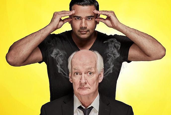 Two performers posing before yellow backdrop one making hypnotic gesture behind other with comic steam effect.