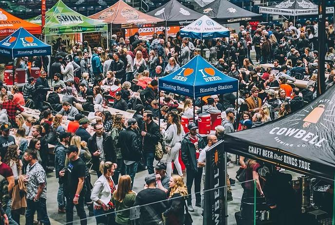 A bustling beer festival in a large indoor space, filled with crowds exploring various colorful vendor tents.