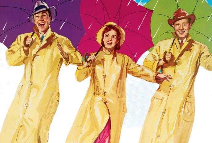 Three people in bright yellow raincoats dance with colorful umbrellas under light rain.