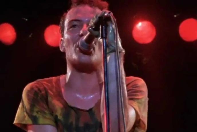 Energetic performer in a multicolored shirt onstage, immersed in their act under intense red lighting. A vibrant scene!