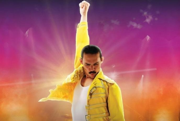 Dynamic stage scene with a performer in a yellow jacket and white outfit, arm raised triumphantly.