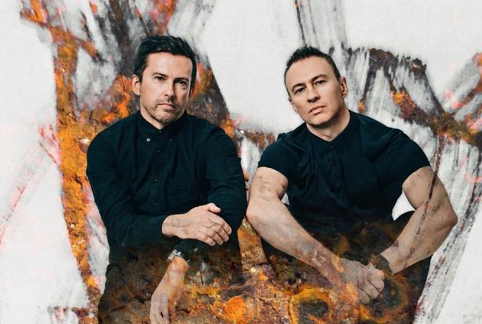 Two men in black shirts sit against a background blending abstract art and earthy textures.