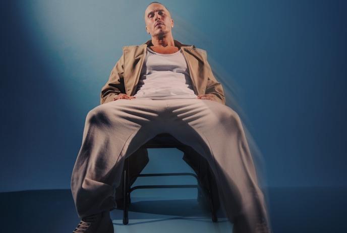Shawn Desman sitting in a chair looking at the camera, in a completely blue room.