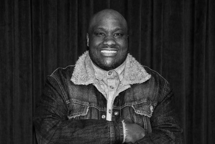 A person wearing a jean jacket with a fur collar smiling at the camera.