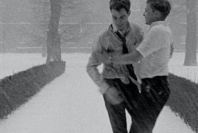Two men in winter clothing engage in conversation on a snowy park pathway surrounded by trees.