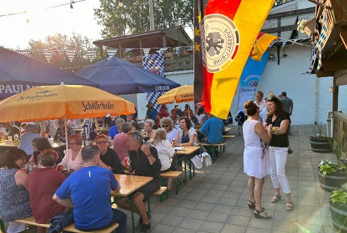 Lively Authentic German Biergarten scene with people dining under German flags.