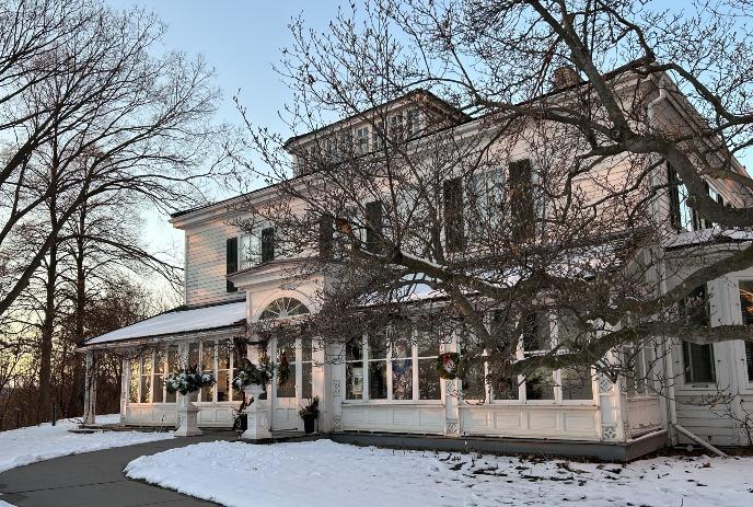 Eldon House with a sunroom, surrounded by bare trees and snow. The early evening sky adds a serene, wintery atmosphere.