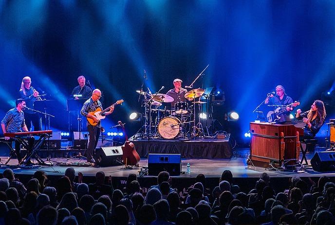 A group of musicians performing on stage under colourful spotlights.