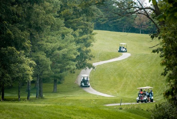 3 golf carts riding up a paved path on a golf course.