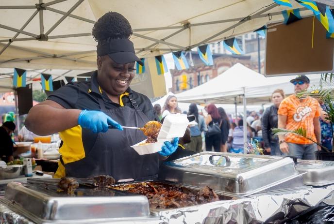 A smiling vendor serves food from a stall at an outdoor festival.