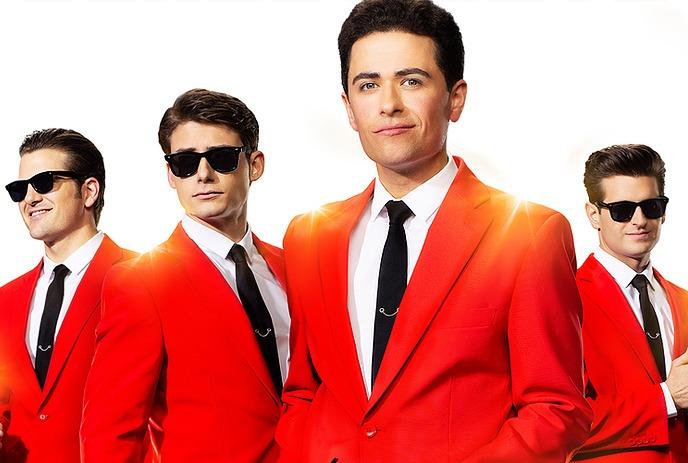 Four artists in red suits white shirts and black ties stand against a white background three wear sunglasses one holds them.