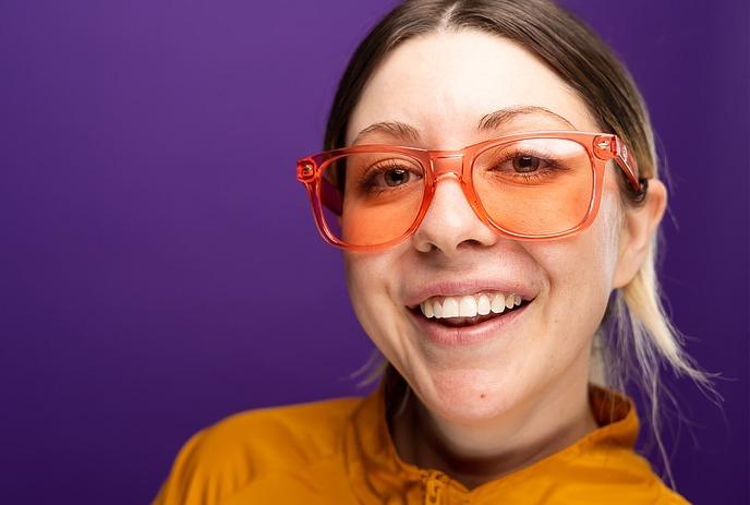 Jessie Johnson smiling for the camera in front of a purple background, wearing orange sunglasses.