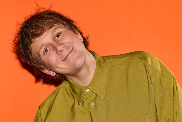 Josh Thomas with his head tilted, looking at the camera and smiling.