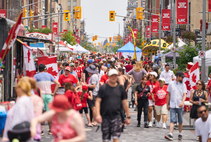 Canada Day street packed with people in red and white, flags waving and tents lining the road