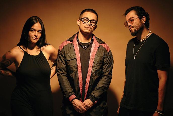 Two men and 1 woman, posing for the camera, lit up against a brown background.