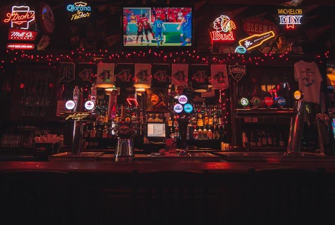 Warm sports bar with neon beer signs, liquor shelves, and a TV showing a soccer match.