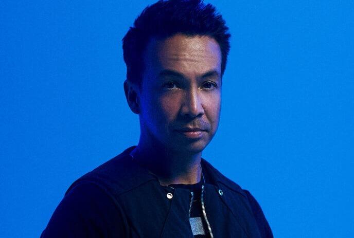 Laidback Luke looking at the camera, wearing a tan jacket in front of a grey background.