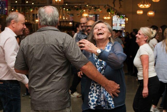 A group of people dancing and laughing together in a warmly lit room.