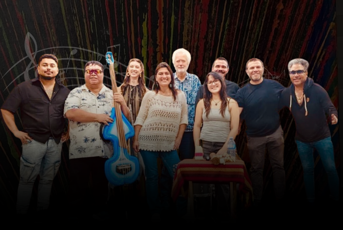 Nine artists stand together with bright blue bass and table of instruments before colorful musical backdrop.