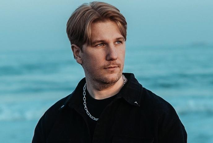 Person in black attire against a swirling abstract backdrop of blue and orange tones.