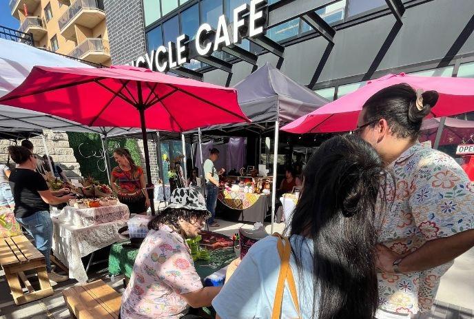 People gather under red umbrellas outside of Bicycle Café for an outdoor market.