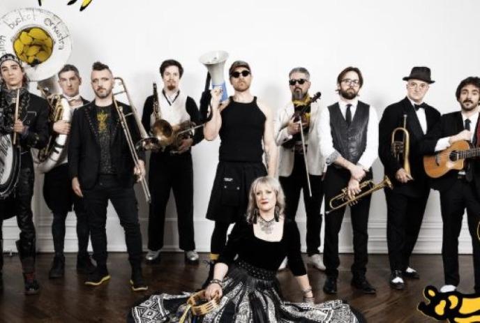 A large band poses indoors with various instruments, including brass, strings, and percussion.