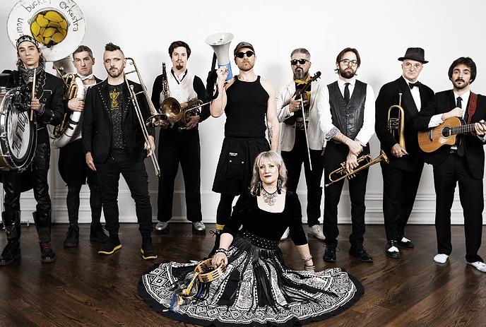 A large band poses indoors with various instruments, including brass, strings, and percussion.