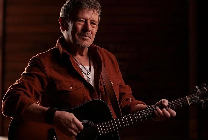 Lennie Gallant holding a guitar, in front of a black background.