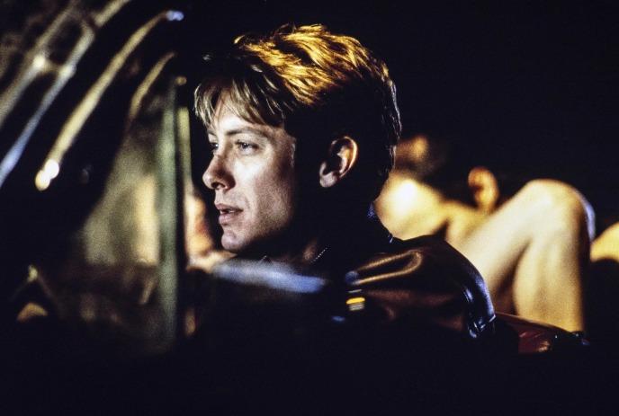 Person in dim car light wearing dark jacket profile lit while another behind.