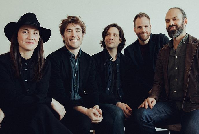 The Five band members of Little Misty sitting, posing for the picture with a yellow wall in the background.