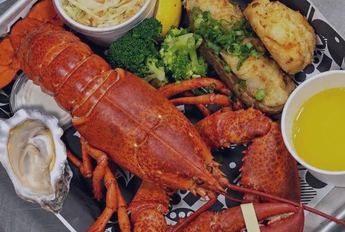 Whole lobster platter with oyster, broccoli, roasted potatoes, slaw, lemon, and melted butter.