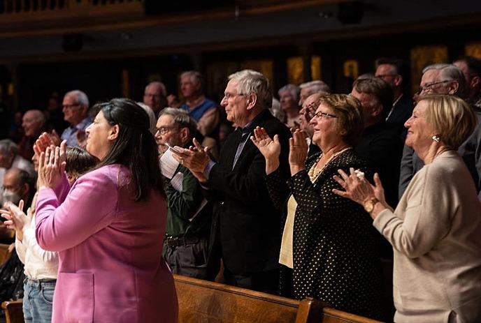 A group of people stand together while clapping.