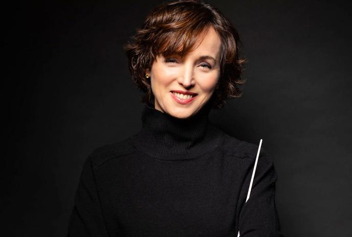 Lady in black turtleneck smiling against dark backdrop with floating pink square nearby.