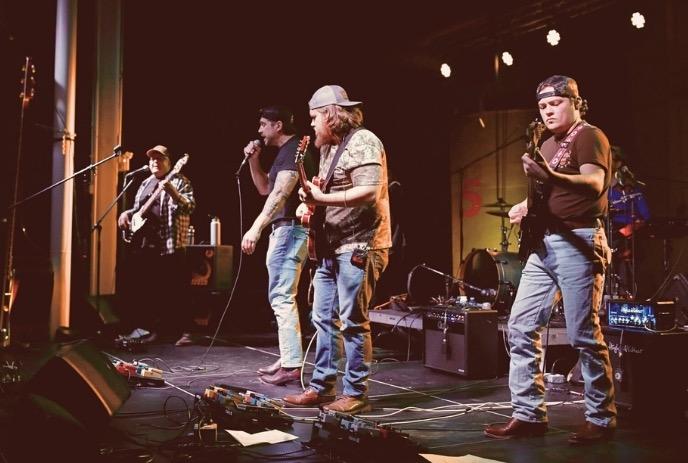Four band members playing their instruments on stage.