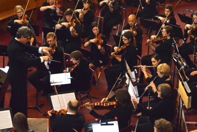 A symphony orchestra performs under the direction of a conductor.