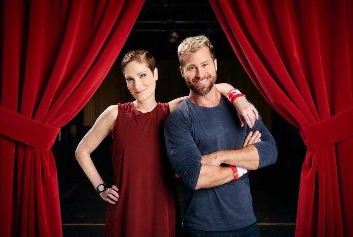 Craig Ramsay and Catherine Wreford standing in front of a red opened theatre curtain, smiling.