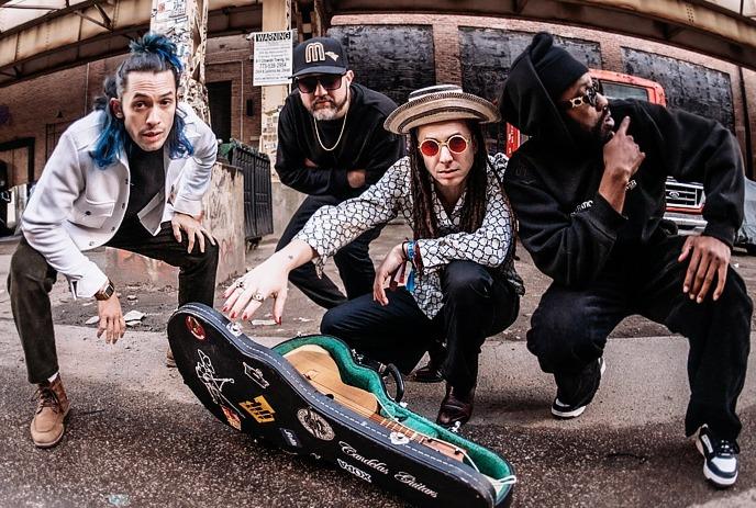 Four musicians pose around an open guitar case beneath an overpass.
