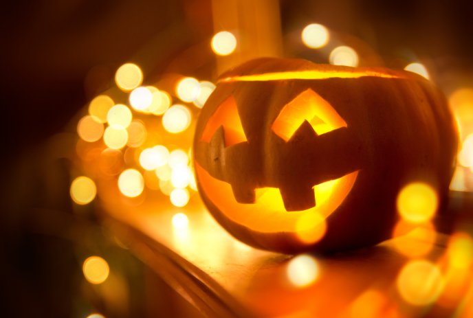 Glowing jack-o'-lantern with carved face, lit from within, surrounded by warm golden fairy lights.