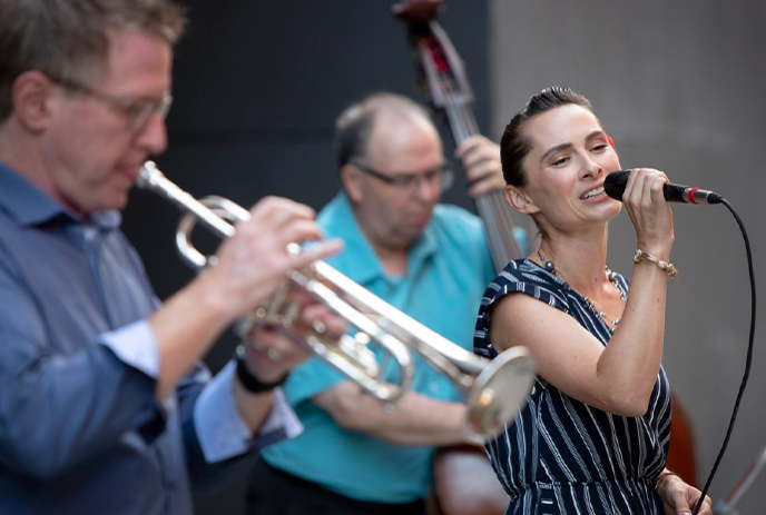 A jazz band performing live, featuring a trumpet, double bass, and a vocalist with a microphone on stage.