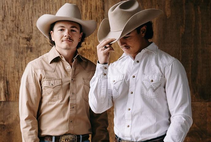 The Martins Boys in cowboy outfits, performing on a dimly green-lit stage, playing their guitars for a crowded audience.