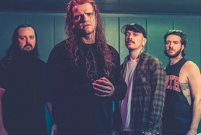 The band Miss May I poses in a dimly lit room with teal walls, illuminated by overhead lights.