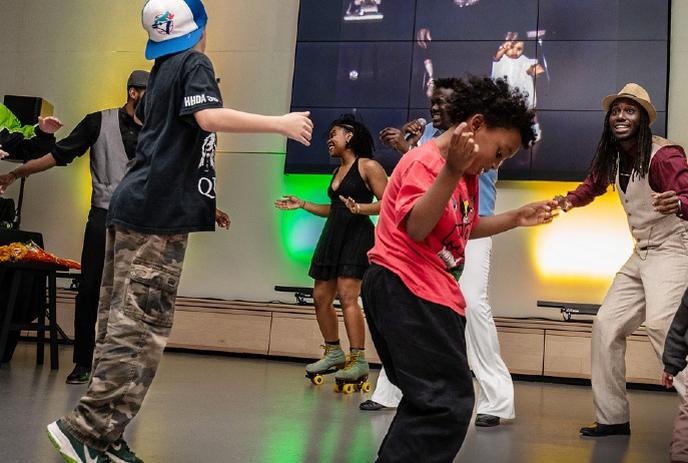 People dancing indoors with kids and adults moving together under bright lights and a large screen.